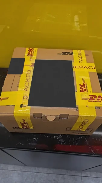 Closed DHL-branded parcel prepared for shipping, with shipping labels and barcodes masked